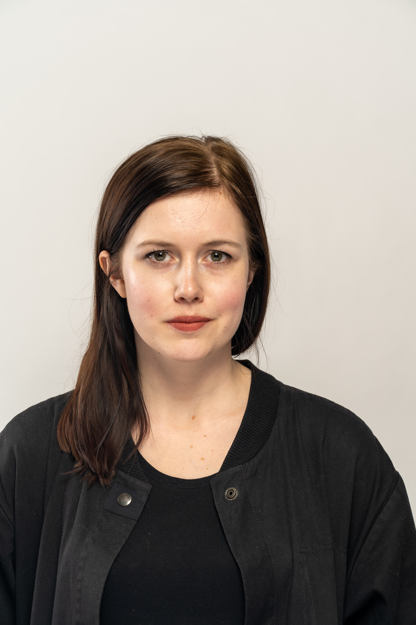 Kaarin Kivirähk, a white-skinned person with long dark brown hair and dark red lipstick. Framed from chest up, Kaarin is wearing a black shirt and a black sweater. Kaarin is standing in front of a white backdrop.