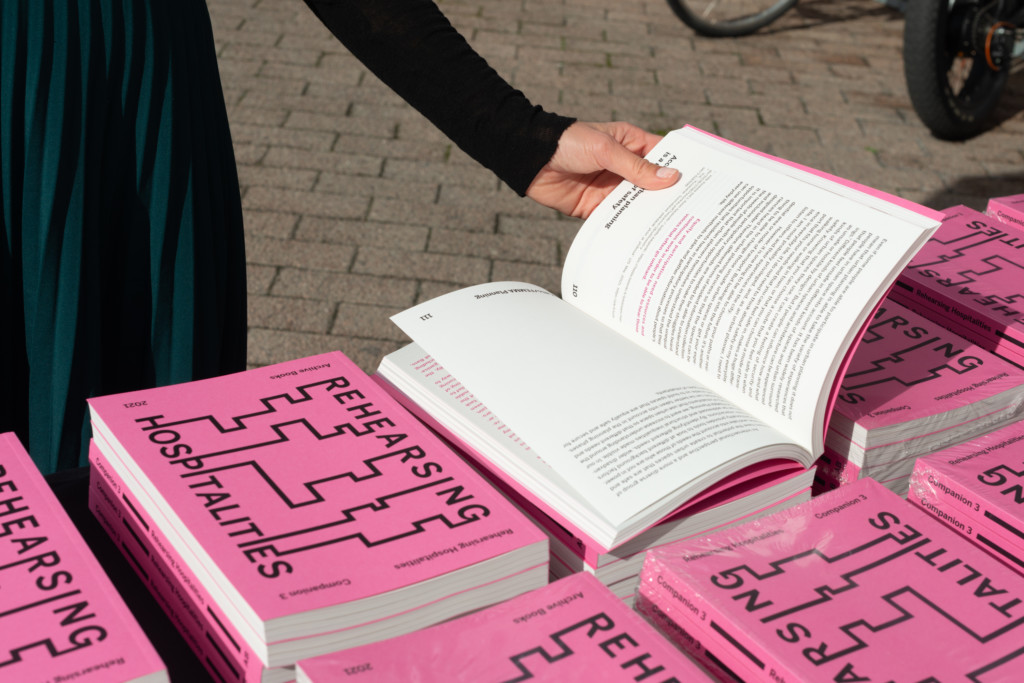 Piles of publication Companion 3 on a table outdoor. There is a hand holding one book open.