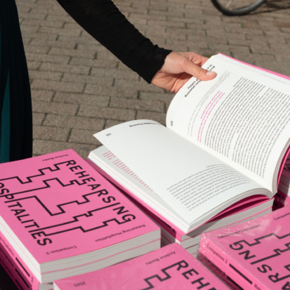Piles of publication Companion 3 on a table outdoor. There is a hand holding one book open.