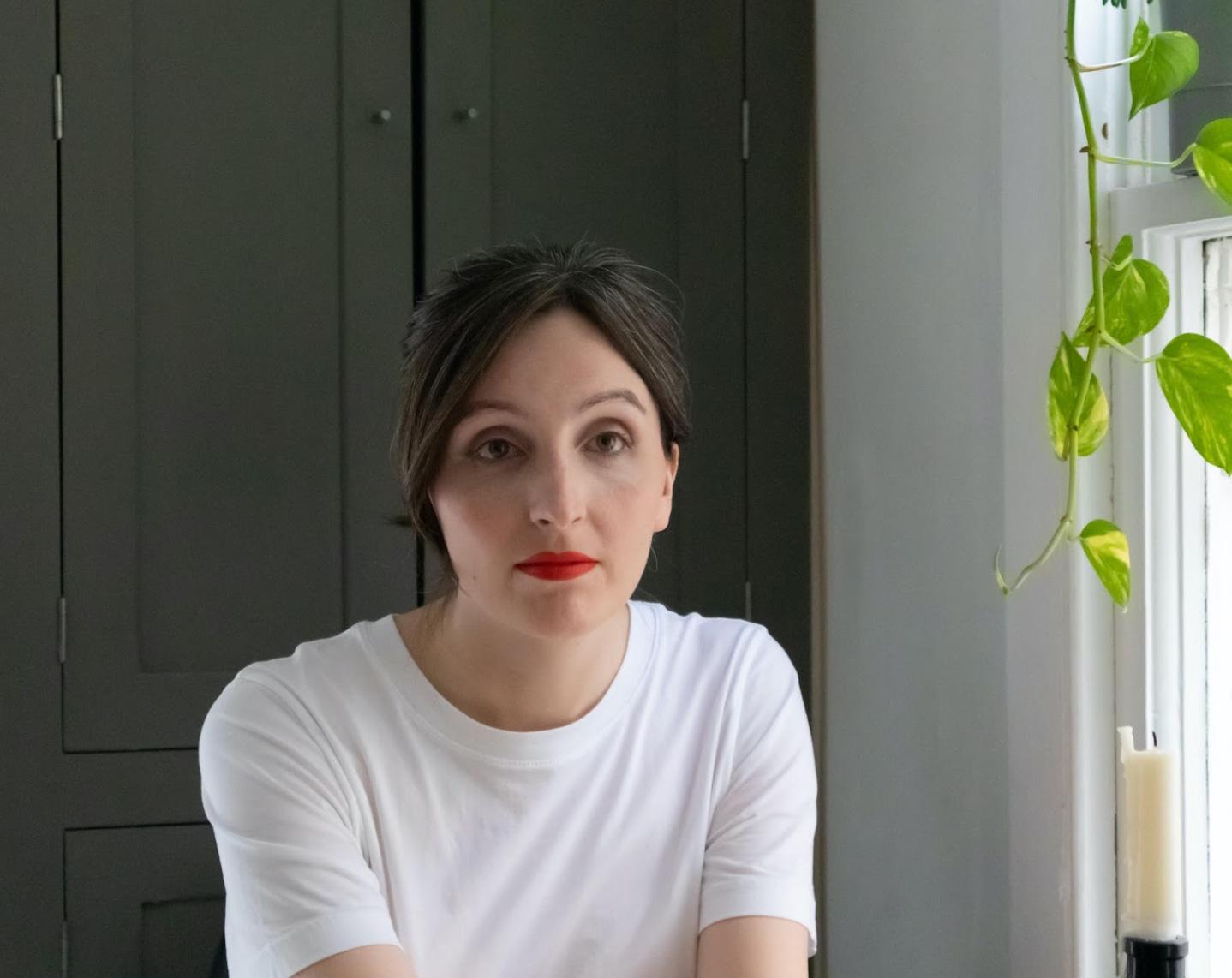 Portrait of a white woman with brown hair and red lipstick in a white t-shirt looking past the camera.