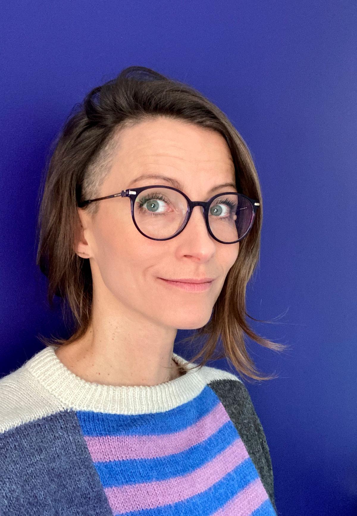 Portrait of a white woman wearing colourful jersey standing against a violet background