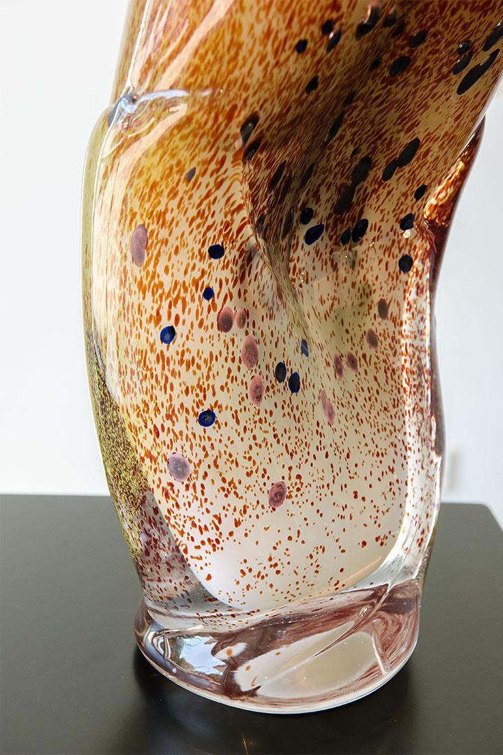 a close-up of a glass vase of organic and undefined shape, focussing on the amber-orange colours and dotted patterns in the blown glass.