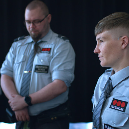 A mid-shot image of three white guards who seem to be listening to something with a serious expression. The guard standing closest to the viewer is the artist Pilvi Takala.