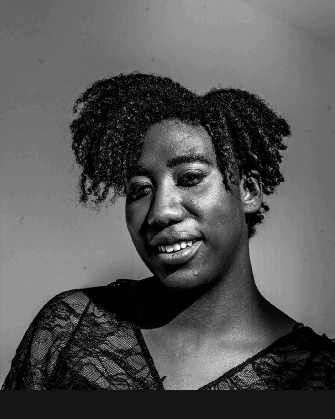 A black and white close-up image of a black person with her head slightly tilted, smiling into the camera.
