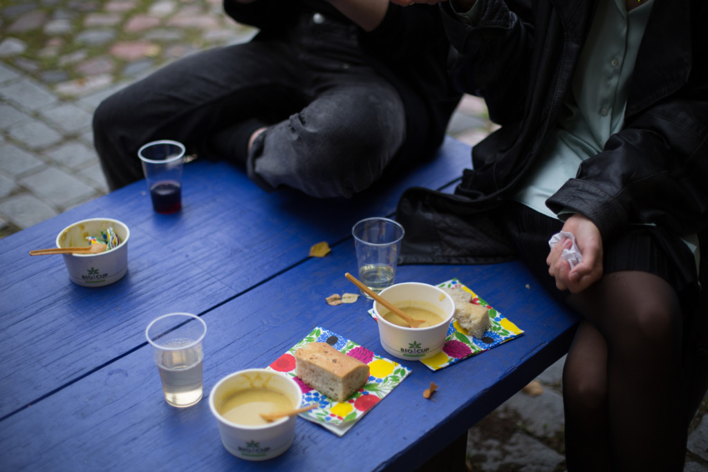 Soup bowls, and pieces of bread and drinks in an outdoor setting on a blue wooden bench. 