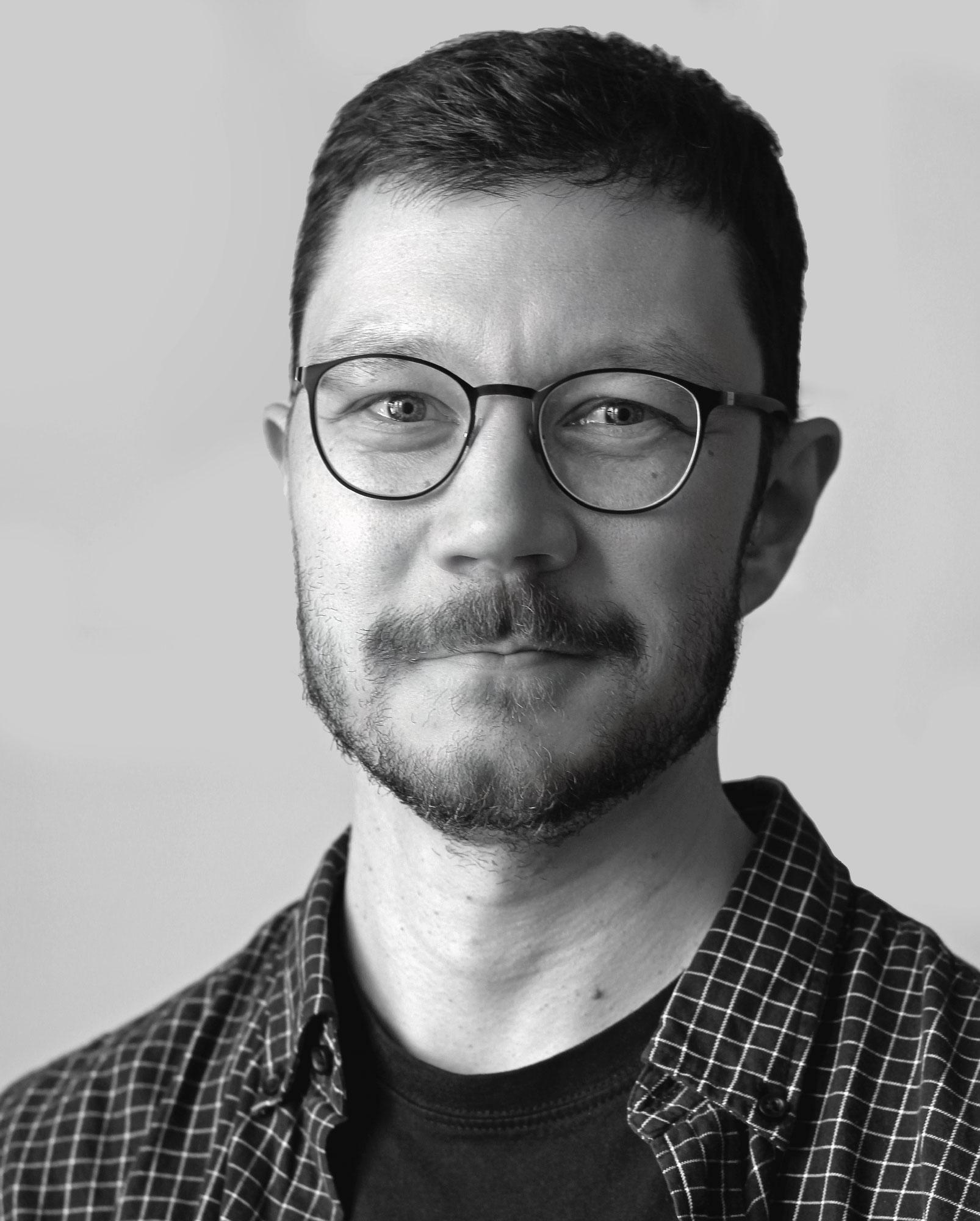 Jaakko Uoti, white man with dark hair and black glasses smiling slightly into the camera