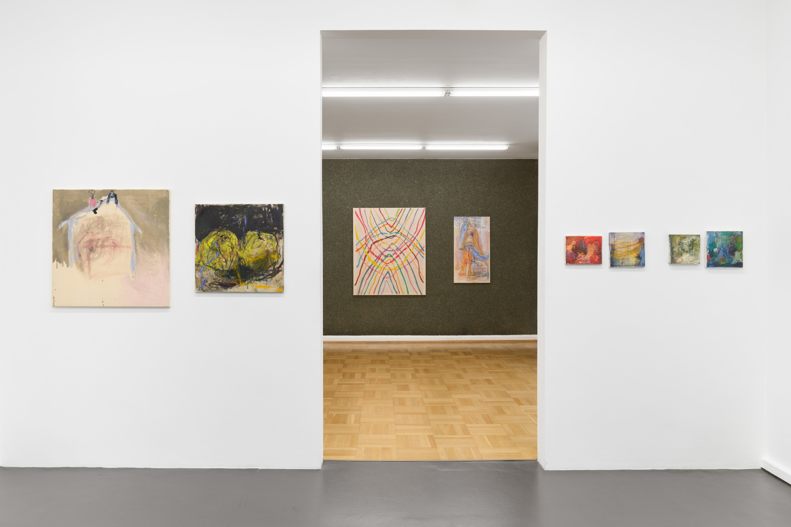 An image of a gallery space: six paintings are hung on the wall in the front. In the middle of the wall is a doorway leading to another room. Two paintings are hung on a wall in the back room.