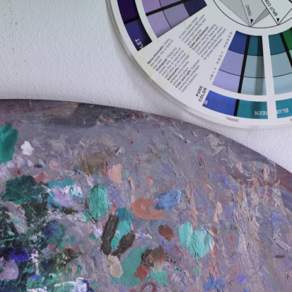 A closeup image of a palette with green, blue, grey and brown paint stains. Next to it is a colour wheel.