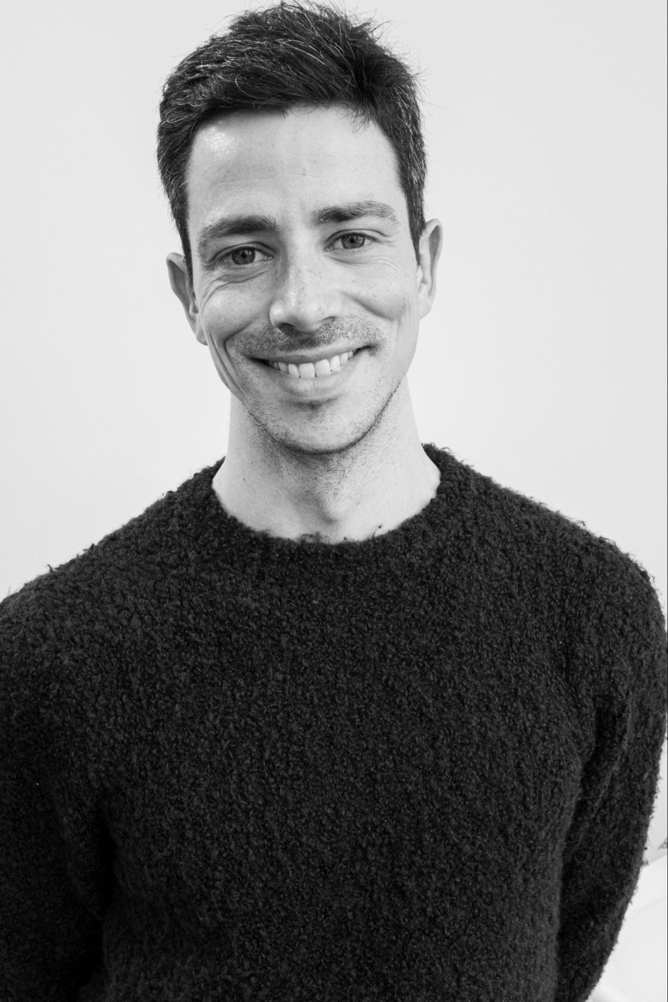 A black and white studio portrait of a person with short hair smiling at the camera.