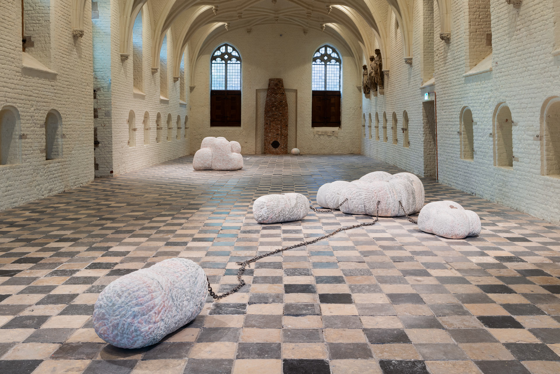 A sculpture installation consisting of four sculptures connected to each other with chains. The marble sculptures have soft shapes.