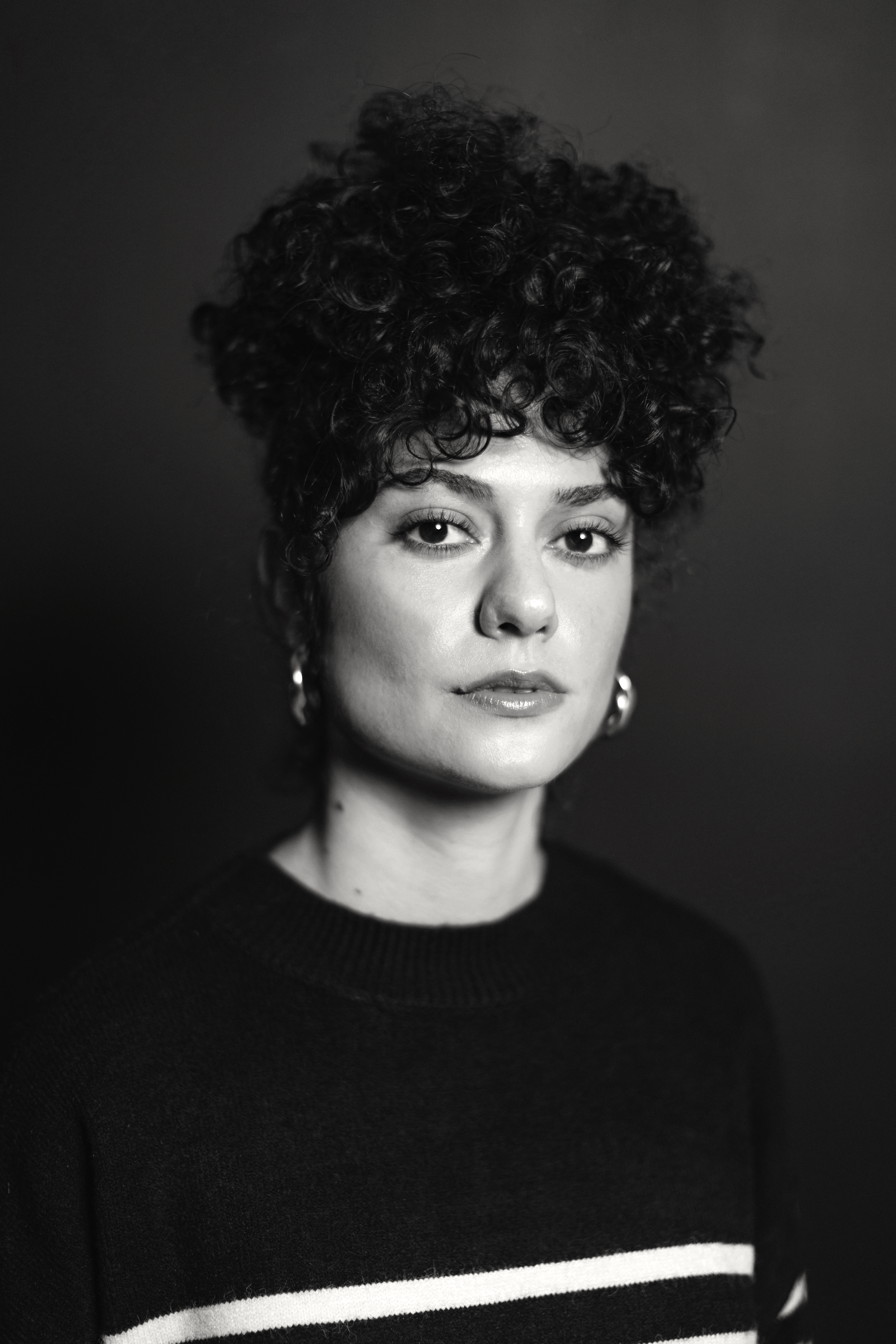 A black and white portrait of a person with light skin and curly dark hair in an updo.
