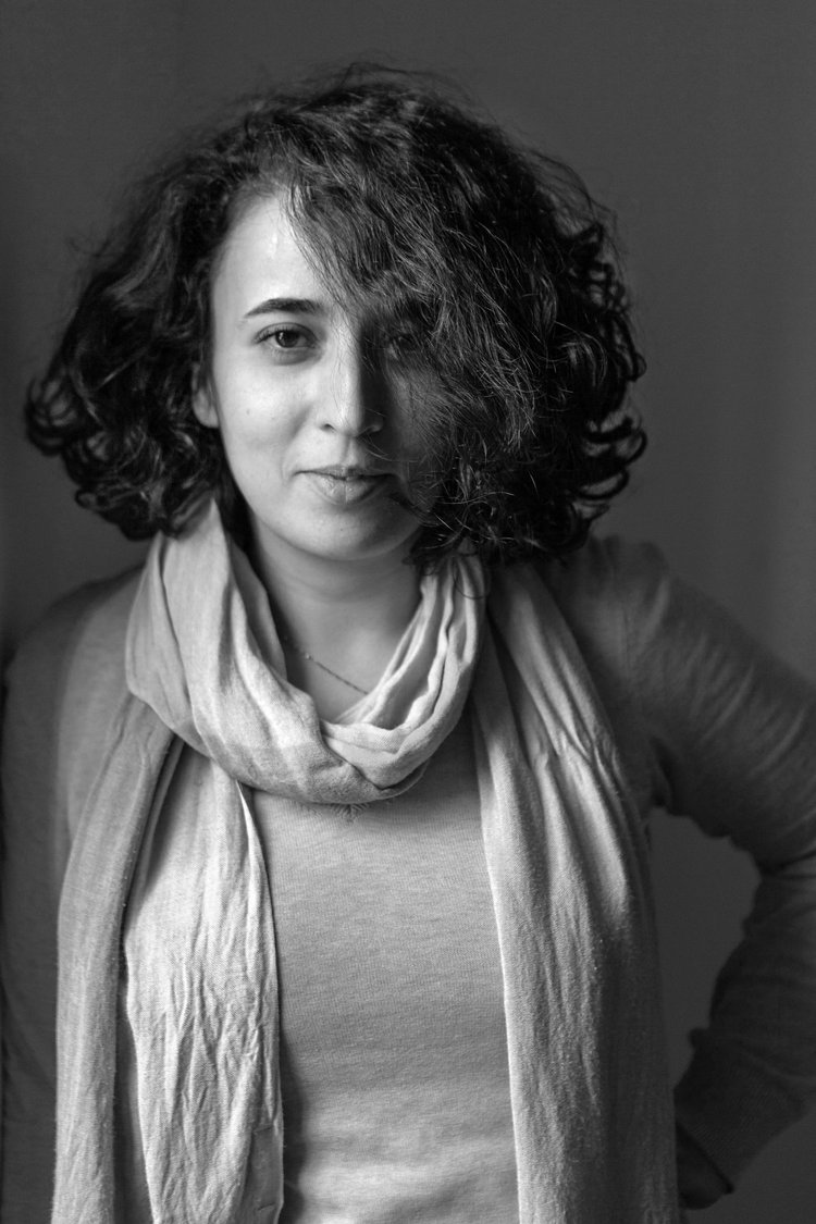 A black and white photo of a person with light skin and half-long dark curly hair wearing a scarf.