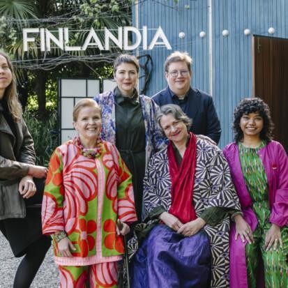 Six people in front of a blue wooden pavilion with a text Finlandia above it.