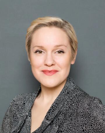 A portrait of the CEO of REFLEX Outi Kuittinen who has a short blonde hair and a black and white patterned jacket.