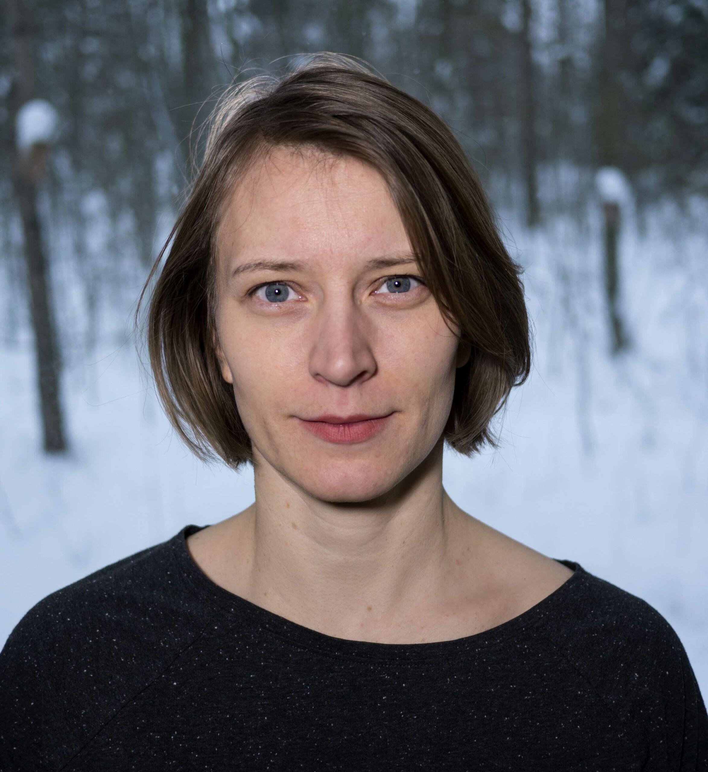 A portrait of a person with a black shirt and short brown hair. In the background you can see a wintery forest.